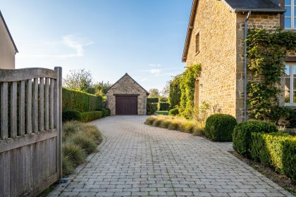 Allée carrossable pavée en béton gris clair menant à un garage avec bordures végétales soignées
