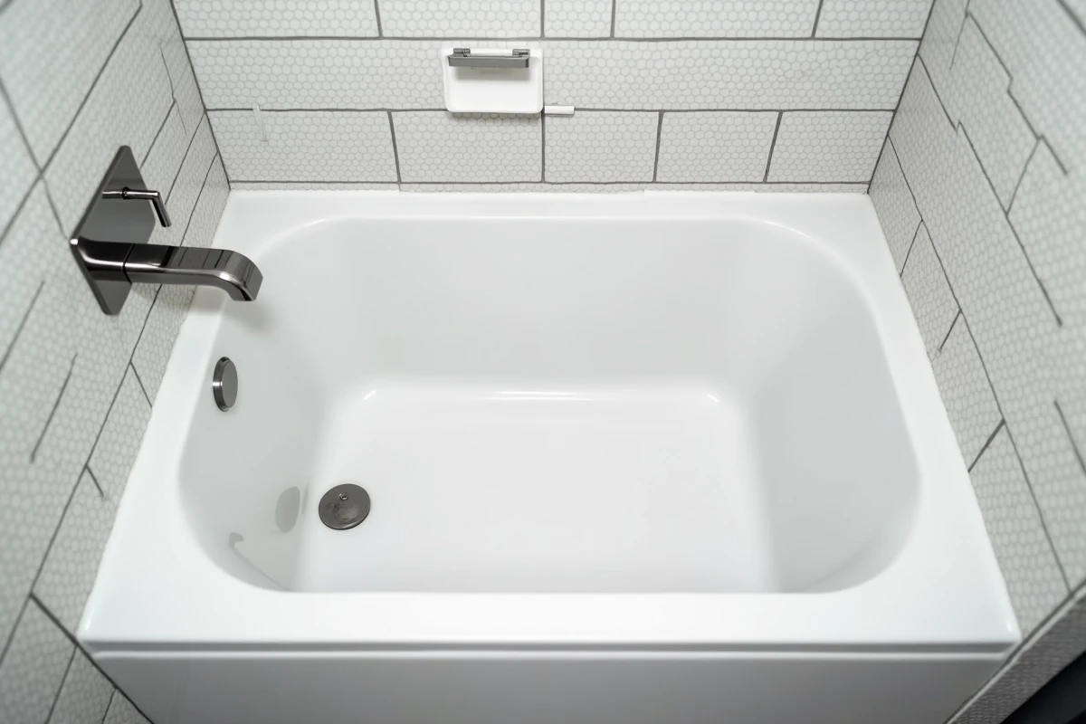 Baignoire encastrée de petite longueur dans une petite salle de bain d'appartement urbain avec carrelage mosaïque blanc