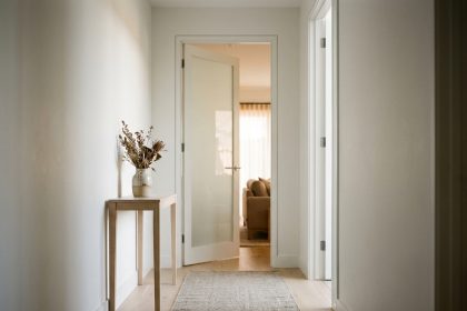 Couloir moderne avec porte battante vitrée en verre dépoli ouverte sur un salon, sol en parquet chêne clair et murs blancs mats