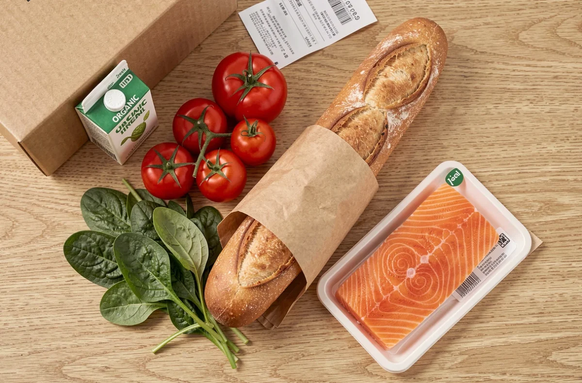 Disposition de produits frais livrés à domicile par Carrefour sur une table en bois, incluant légumes, pain et poisson